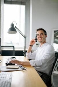 pexels-photo-8867238-8867238 A cheerful call center agent wearing headphones works at a modern office desk.